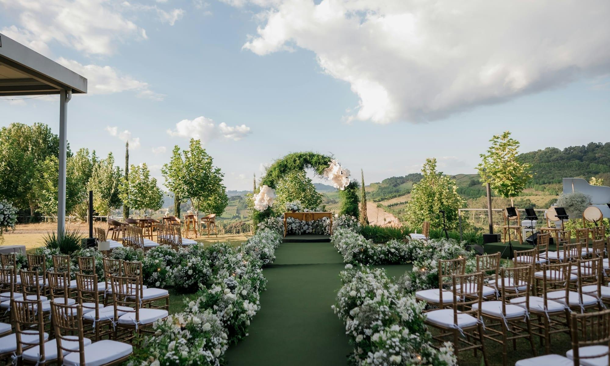 Outdoor ceremony seating facing a floral arch on a hillside lawn